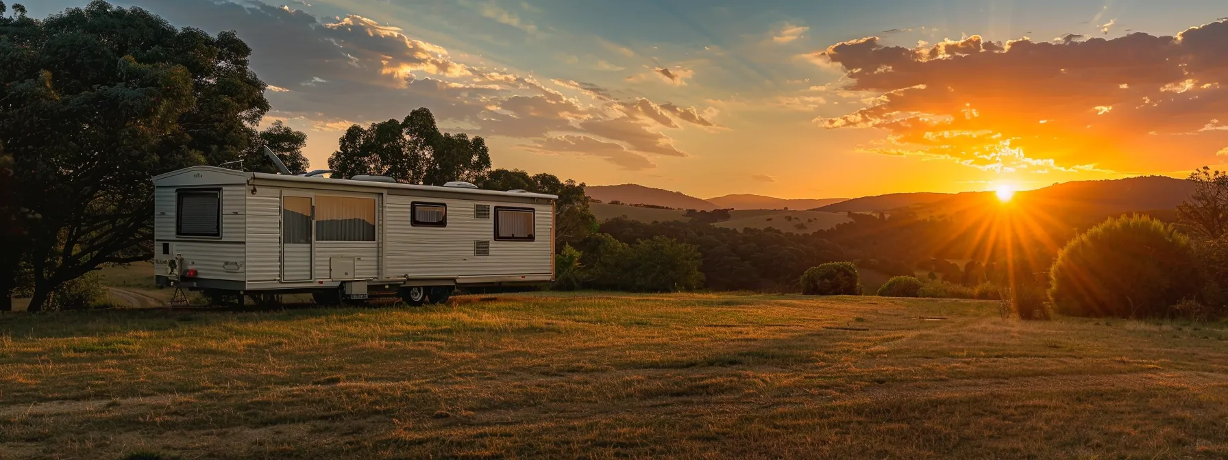 a vibrant sunset casts a warm glow over a serene landscape featuring a sleek mobile home being expertly maneuvered into position by a professional mover, showcasing the art of relocation amidst the tranquil surroundings.
